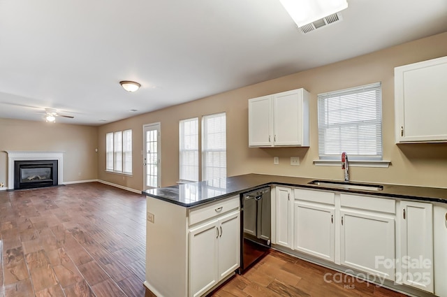 kitchen with dark countertops, visible vents, a sink, dishwasher, and a peninsula