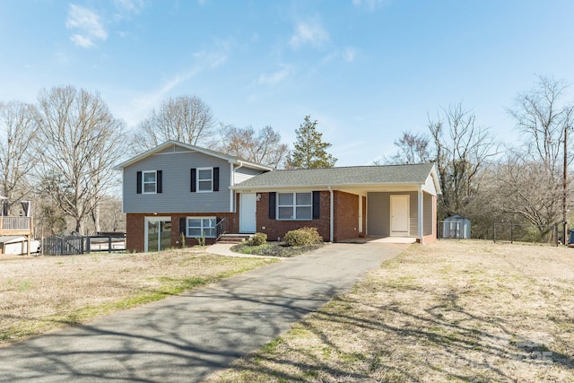 split level home with driveway, an outbuilding, fence, a storage unit, and brick siding