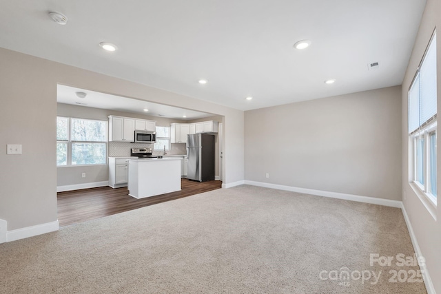 kitchen with stainless steel appliances, dark colored carpet, open floor plan, and white cabinetry