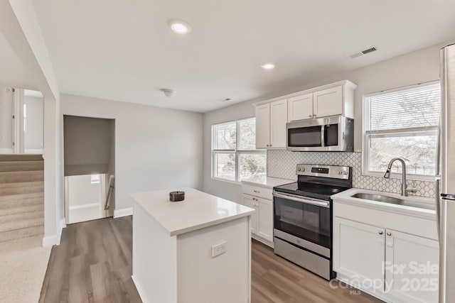 kitchen featuring tasteful backsplash, visible vents, a kitchen island, stainless steel appliances, and a sink