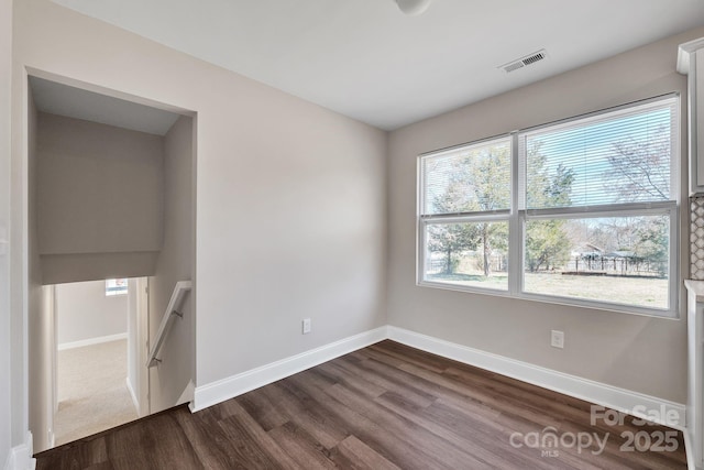 unfurnished room with dark wood-style flooring, visible vents, and baseboards