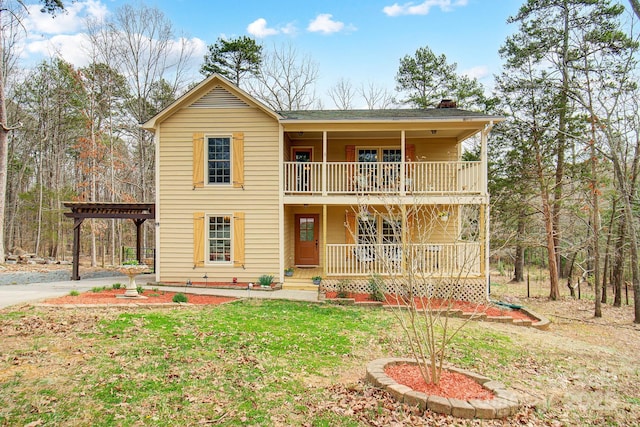 view of front of property with covered porch, a front lawn, a chimney, and a balcony