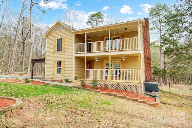 view of property with cooling unit, a balcony, covered porch, a front lawn, and a chimney