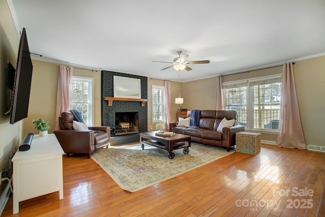 living room featuring light wood-style floors, ceiling fan, a brick fireplace, and ornamental molding