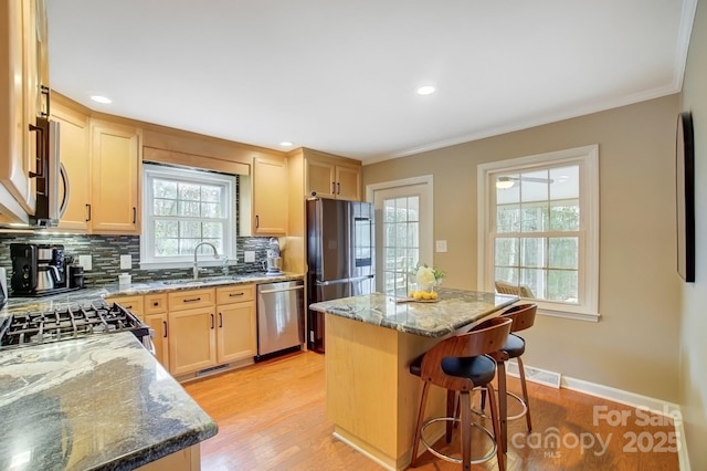 kitchen featuring stone countertops, appliances with stainless steel finishes, a sink, light brown cabinetry, and backsplash