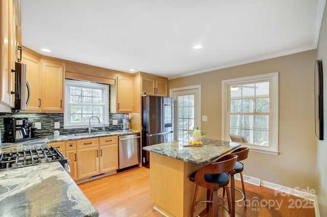 kitchen with stainless steel appliances, a kitchen breakfast bar, light wood-style floors, backsplash, and light stone countertops