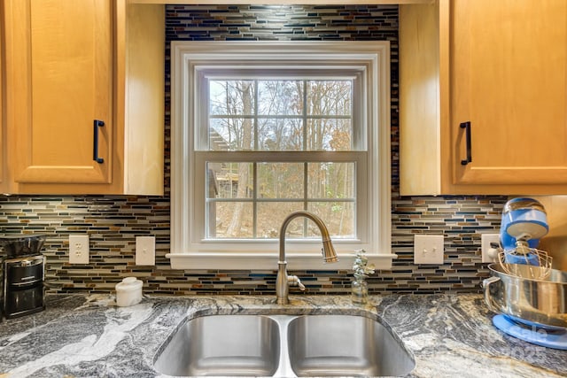 kitchen featuring tasteful backsplash, stone counters, and a sink