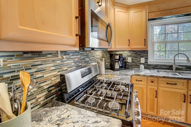 kitchen featuring light stone counters, a sink, appliances with stainless steel finishes, decorative backsplash, and light brown cabinetry