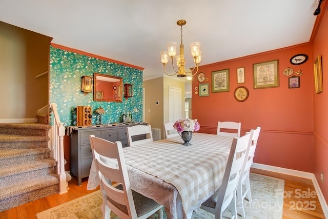 dining room with an accent wall, crown molding, baseboards, and wallpapered walls