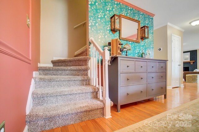 stairway featuring an accent wall, wood finished floors, crown molding, and wallpapered walls