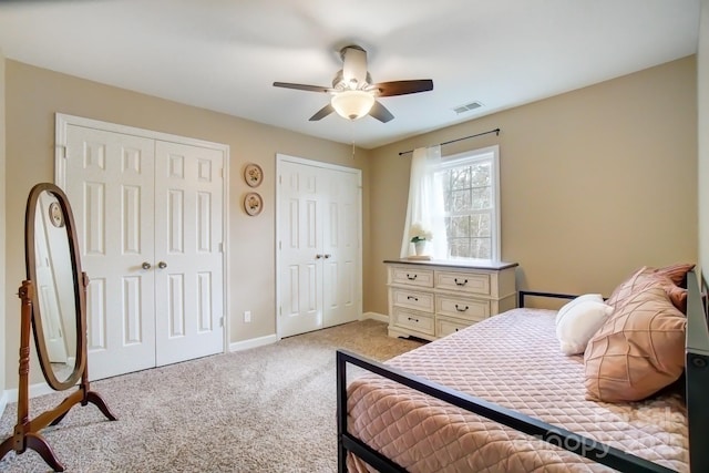 bedroom featuring light carpet, baseboards, visible vents, a ceiling fan, and multiple closets