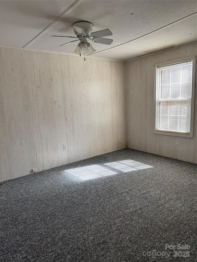 empty room with a textured ceiling, ceiling fan, carpet flooring, and wooden walls