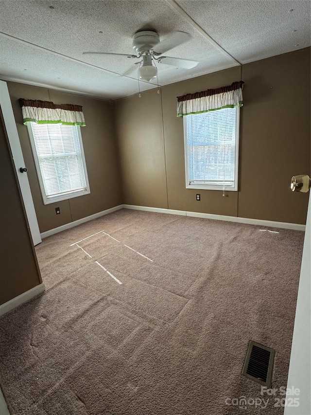 carpeted empty room featuring baseboards, visible vents, ceiling fan, and a textured ceiling