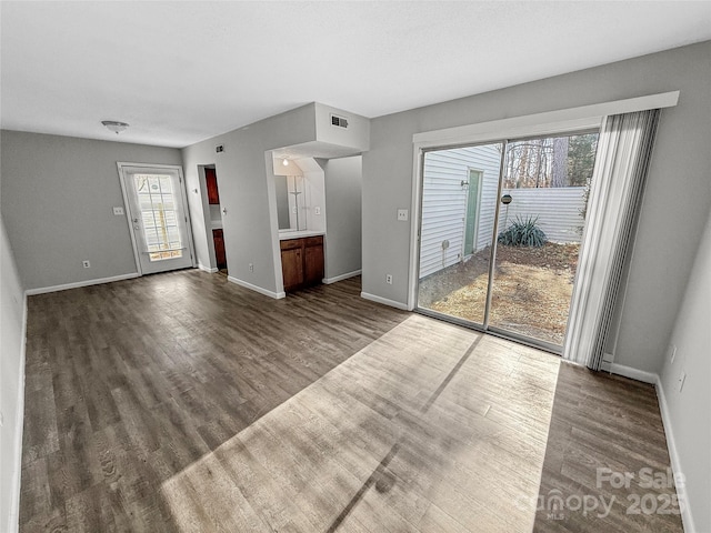 unfurnished living room featuring dark wood-type flooring, visible vents, and baseboards