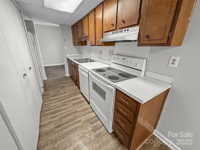 kitchen featuring under cabinet range hood, white appliances, light wood-style floors, light countertops, and brown cabinetry