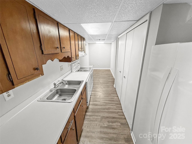 kitchen with light wood finished floors, brown cabinetry, light countertops, a paneled ceiling, and white range with electric cooktop