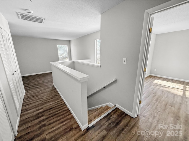 hallway with dark wood finished floors, visible vents, a textured ceiling, an upstairs landing, and baseboards