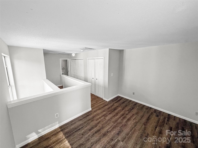 unfurnished room featuring a textured ceiling, wood finished floors, visible vents, and baseboards