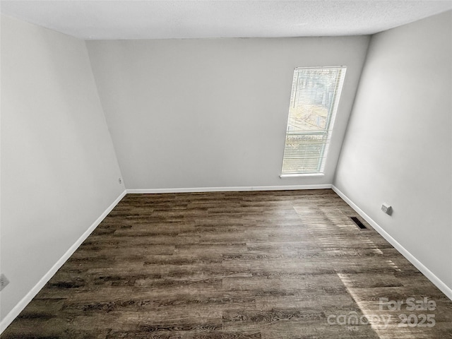 empty room with dark wood-style floors, visible vents, baseboards, and a textured ceiling