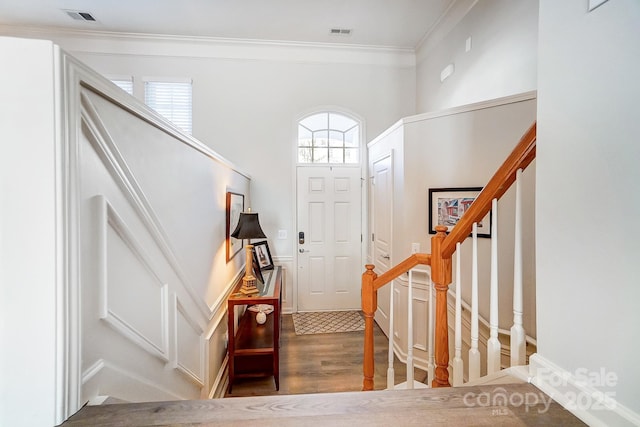 entryway with ornamental molding, wood finished floors, visible vents, and stairs