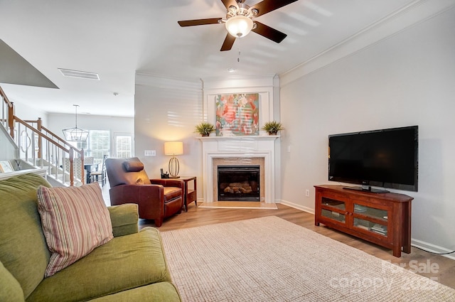 living area with visible vents, stairway, wood finished floors, a fireplace, and ceiling fan with notable chandelier