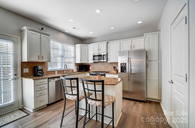 kitchen with stainless steel appliances, visible vents, white cabinetry, a sink, and a kitchen island