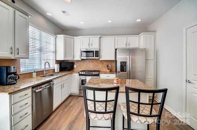 kitchen with stainless steel appliances, light stone counters, a sink, and white cabinetry