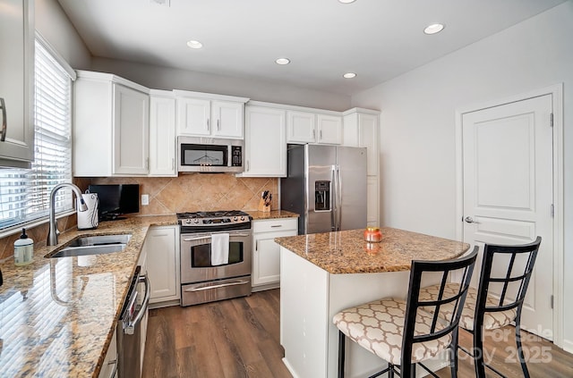 kitchen featuring light stone counters, appliances with stainless steel finishes, white cabinetry, a sink, and a kitchen bar