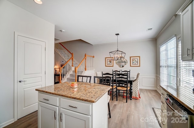 kitchen with pendant lighting, light wood finished floors, visible vents, a kitchen island, and light stone countertops