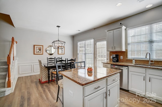 kitchen with a center island, pendant lighting, a sink, light stone countertops, and dishwasher