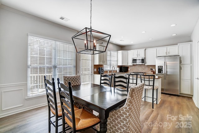 dining area featuring visible vents, a wainscoted wall, light wood-style flooring, crown molding, and recessed lighting