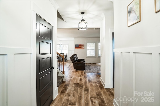 hall featuring dark wood-type flooring, stairway, wainscoting, an inviting chandelier, and crown molding