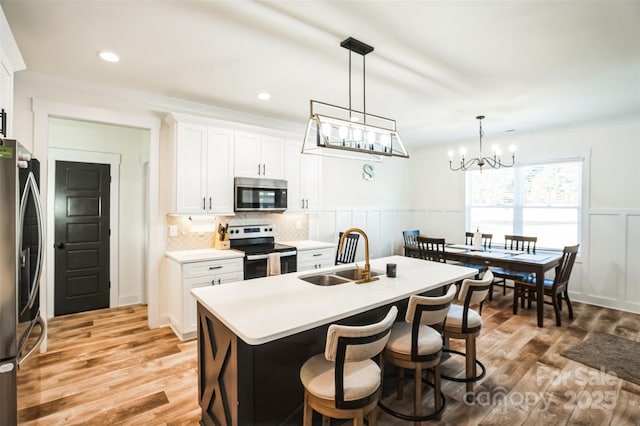 kitchen featuring a wainscoted wall, appliances with stainless steel finishes, light wood finished floors, and a sink