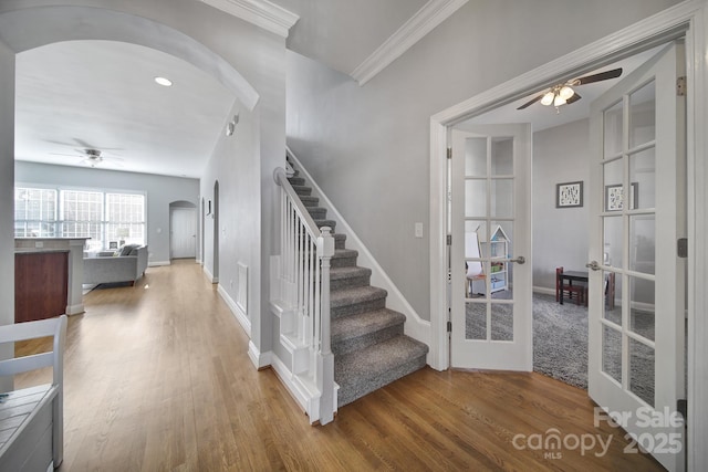 stairway featuring arched walkways, french doors, crown molding, a ceiling fan, and wood finished floors