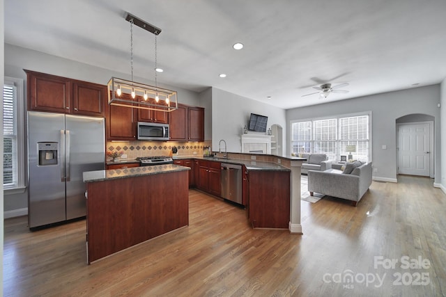 kitchen with arched walkways, stainless steel appliances, a peninsula, a sink, and open floor plan