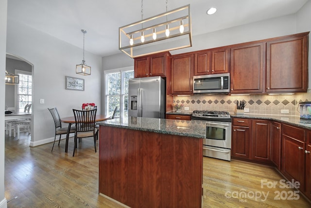 kitchen with appliances with stainless steel finishes, light wood-style floors, backsplash, and a kitchen island