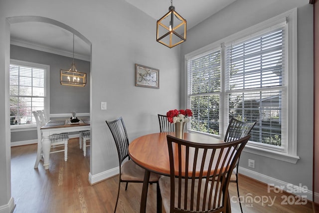 dining space with arched walkways, crown molding, a notable chandelier, wood finished floors, and baseboards