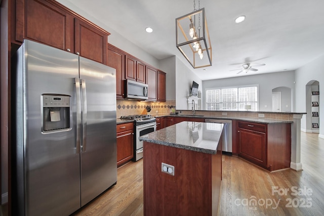 kitchen featuring appliances with stainless steel finishes, a center island, a peninsula, dark brown cabinets, and a sink