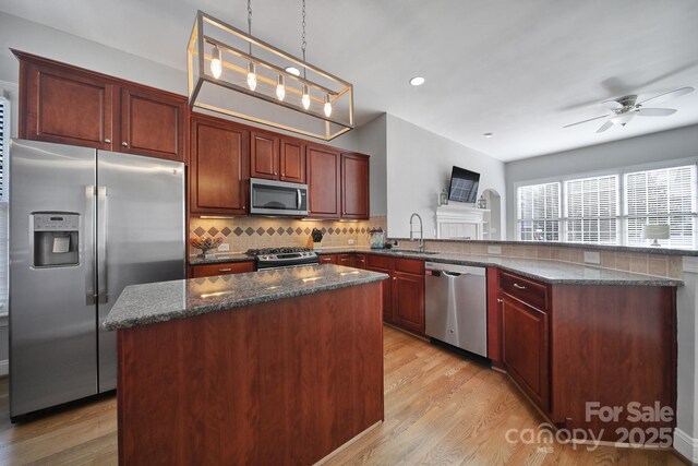 kitchen featuring light wood finished floors, decorative backsplash, a peninsula, stainless steel appliances, and a sink