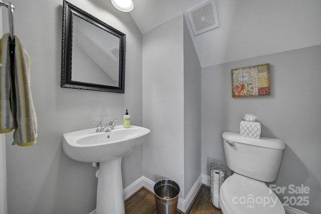 half bath featuring baseboards, visible vents, toilet, wood finished floors, and vaulted ceiling