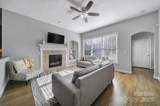 living area featuring a ceiling fan, visible vents, baseboards, light wood finished floors, and a tiled fireplace