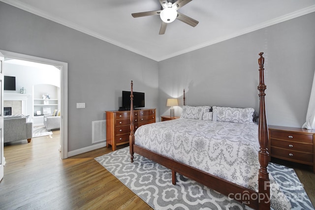 bedroom with a tiled fireplace, visible vents, wood finished floors, and ornamental molding