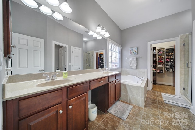 bathroom featuring a garden tub, a sink, double vanity, a stall shower, and a walk in closet