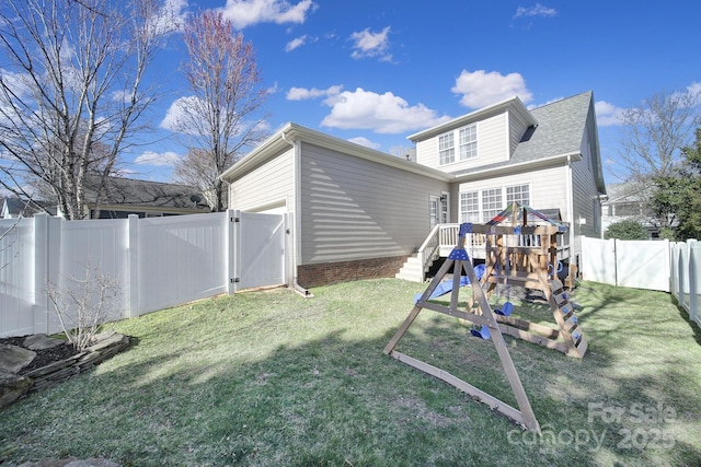 back of house with a playground, a fenced backyard, a garage, a yard, and a gate