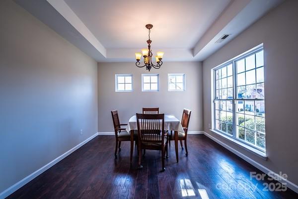 dining room with dark wood-style floors, a tray ceiling, visible vents, and baseboards