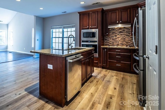 kitchen with light wood finished floors, tasteful backsplash, stainless steel appliances, under cabinet range hood, and a sink