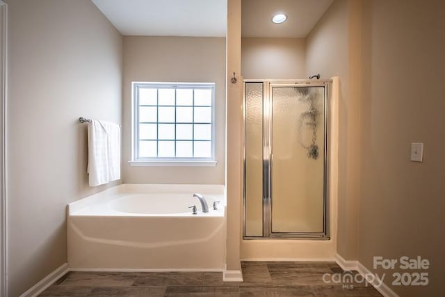 full bathroom featuring a stall shower, wood finished floors, baseboards, and a bath