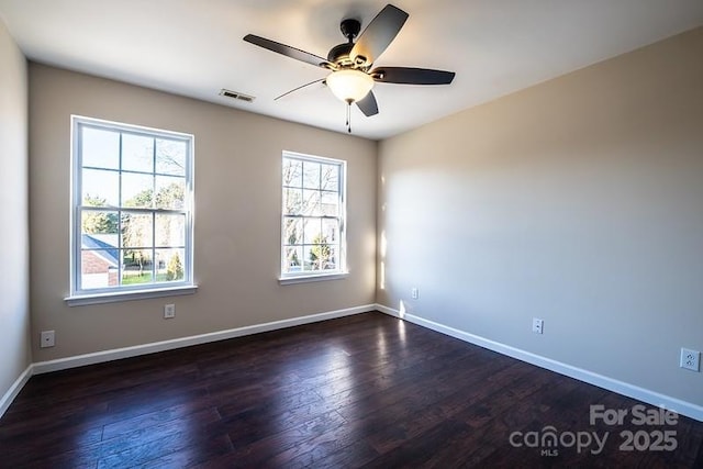 empty room featuring dark wood-type flooring, visible vents, and baseboards