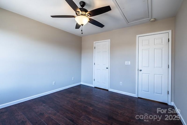 unfurnished bedroom with a ceiling fan, attic access, baseboards, and dark wood-style flooring