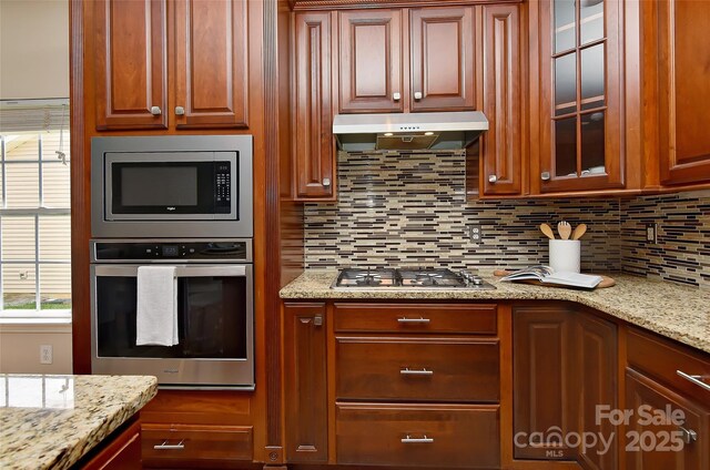 2017 Bridleside Dr, Indian Trail, NC 28079 - kitchen featuring appliances with stainless steel finishes, under cabinet range hood, backsplash, and glass insert cabinets